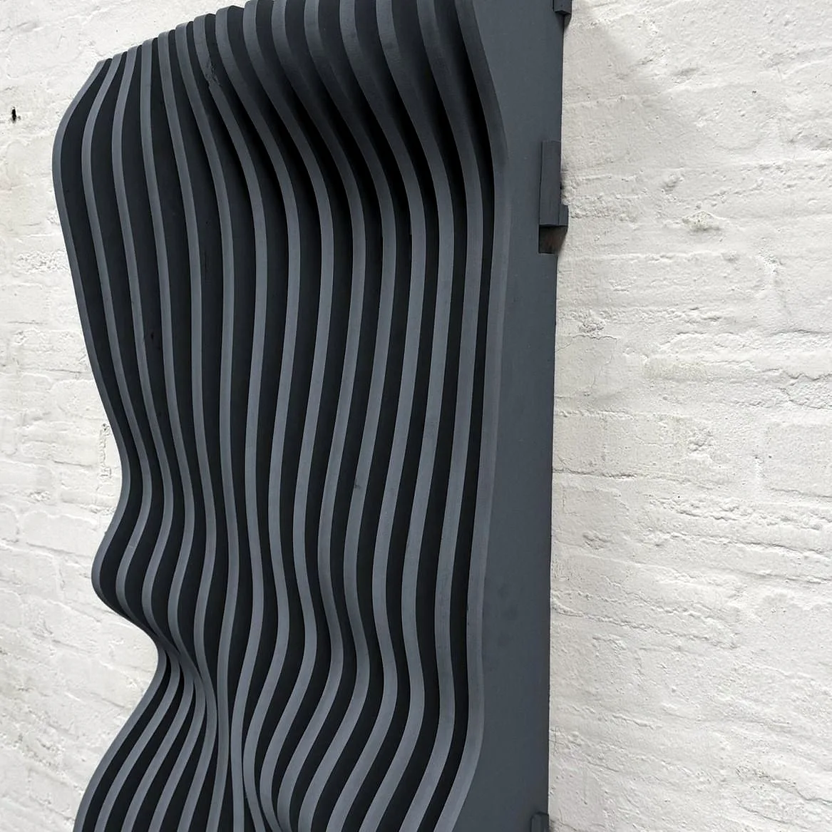 A ripple wall of routed MDF fins in anthracite grey, fitted to a brick wall